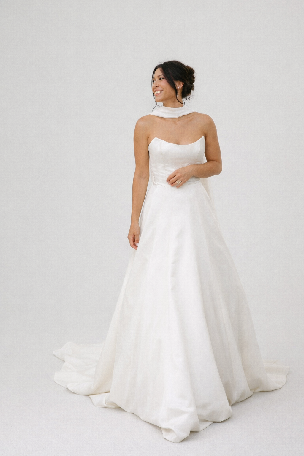 Woman wearing a strapless white wedding dress on a plain background